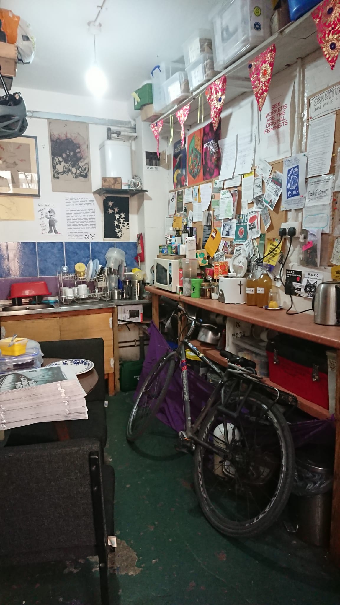 A photo of the kitchen, with a bike parked in it. There is a microwave, kettle, toaster and sink.